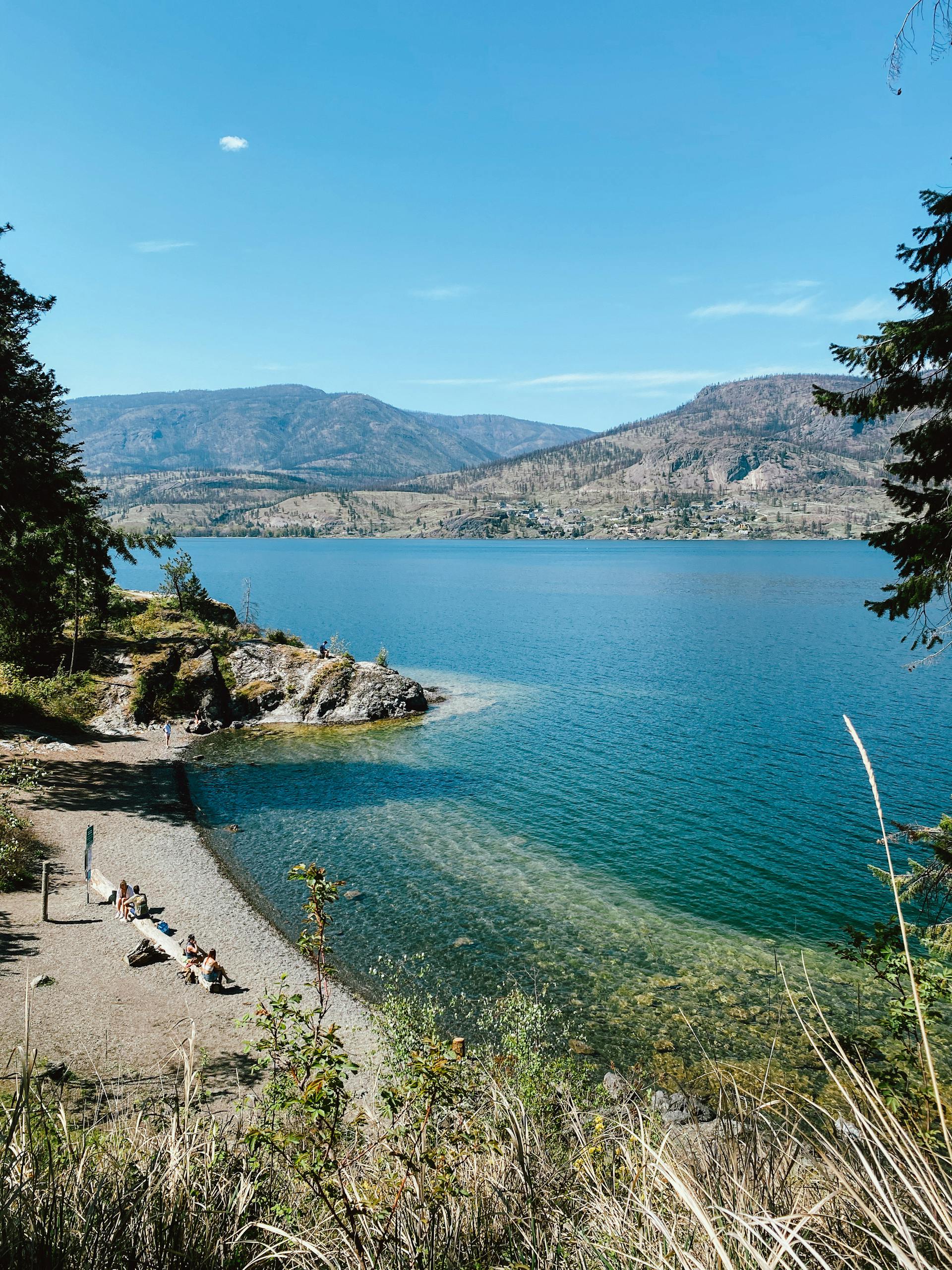 Beautiful view of Okanagan Lake and mountains from a sunny park in Kelowna, perfect for relaxation.